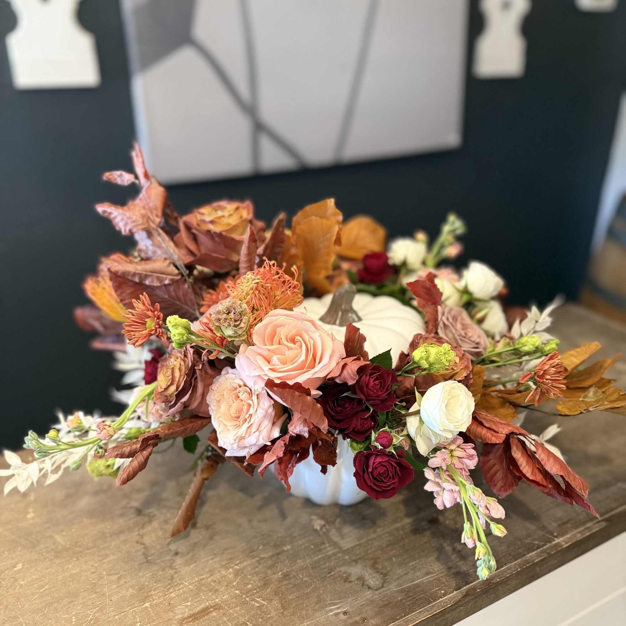 Low floral centerpiece in a white pumpkin container with roses and autumn leaves