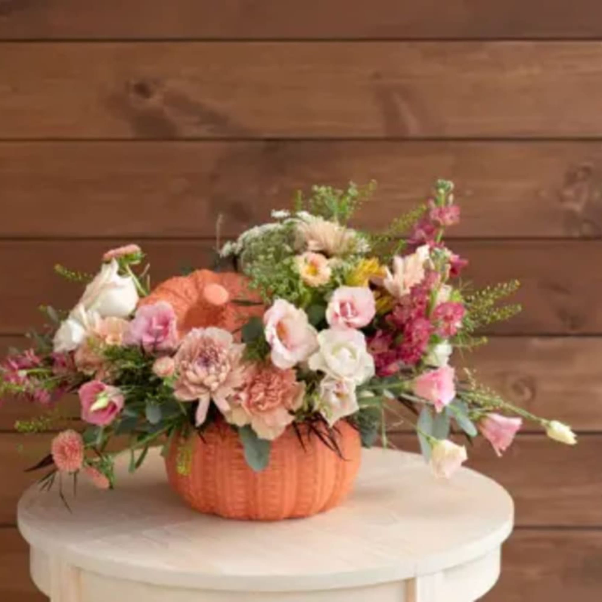 Mixed pink and white flowers arranged in an orange pumpkin container