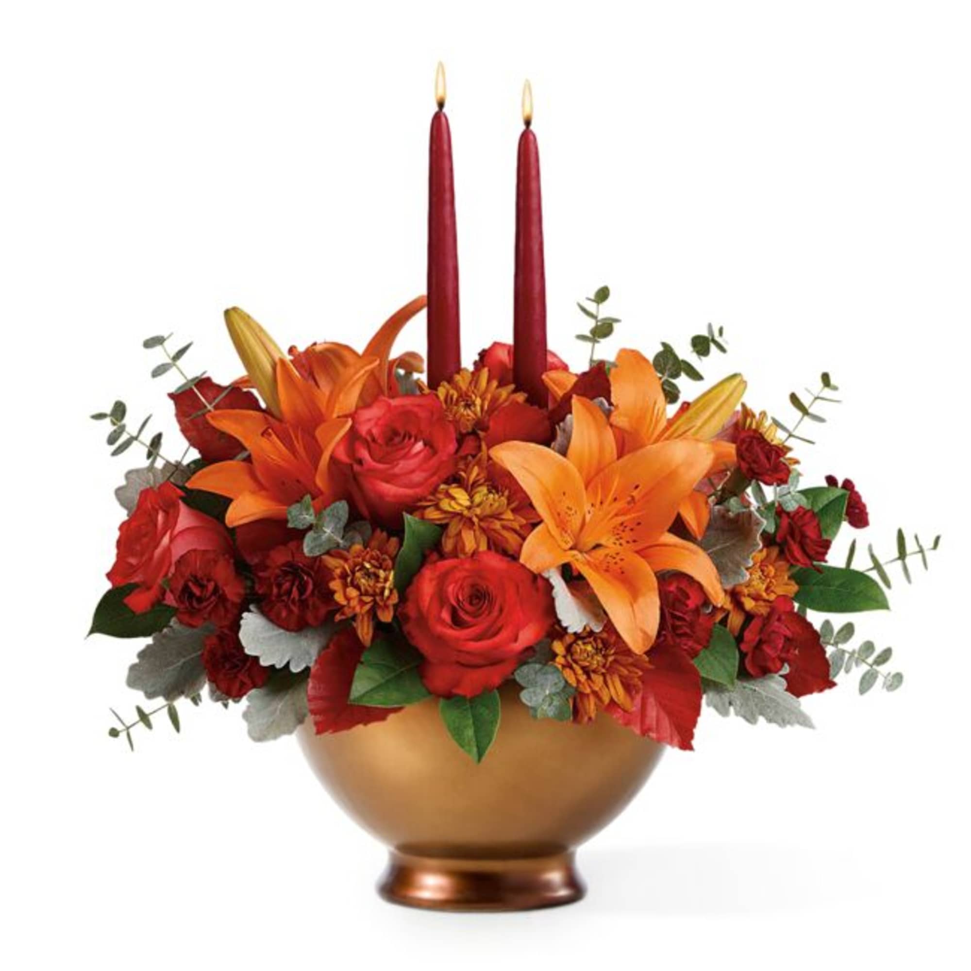 Red and orange floral arrangement in a gold bowl with two burgundy candles