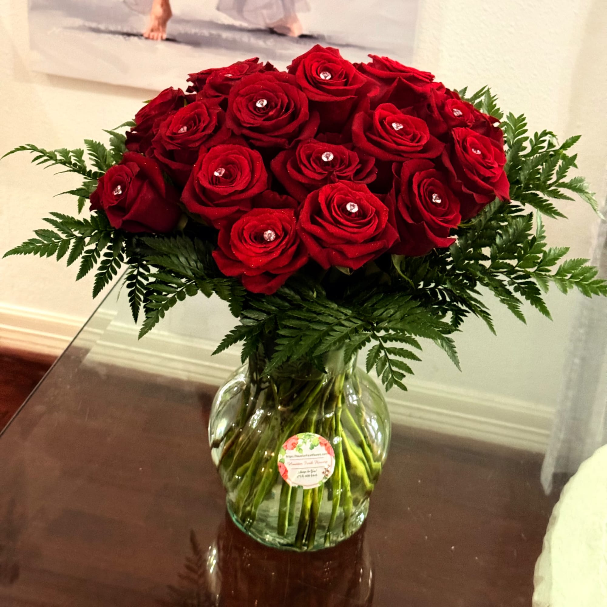 Red roses arranged in a clear glass vase with fern foliage