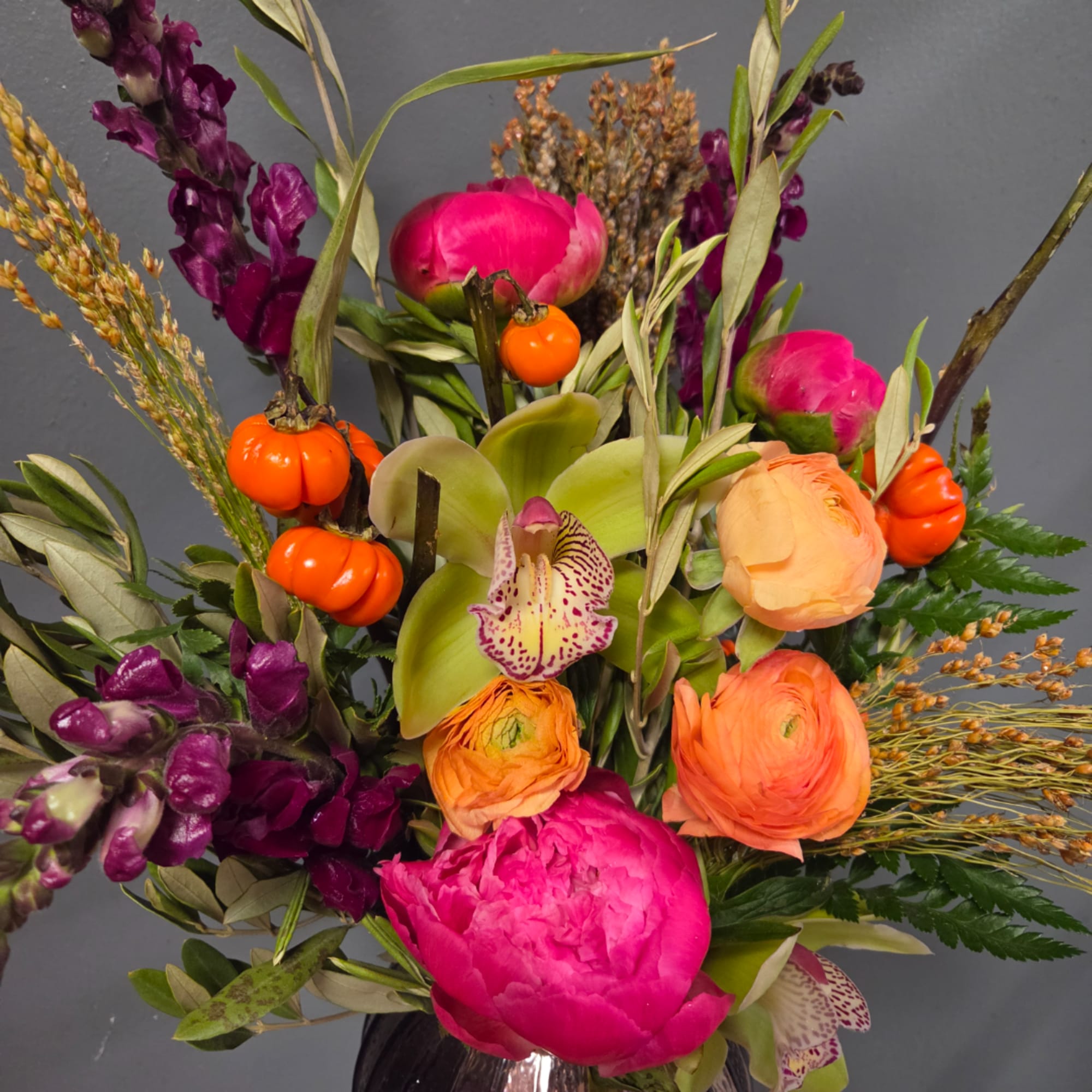Bright mixed bouquet with pink peonies, orange ranunculus, and purple snapdragons in a vase