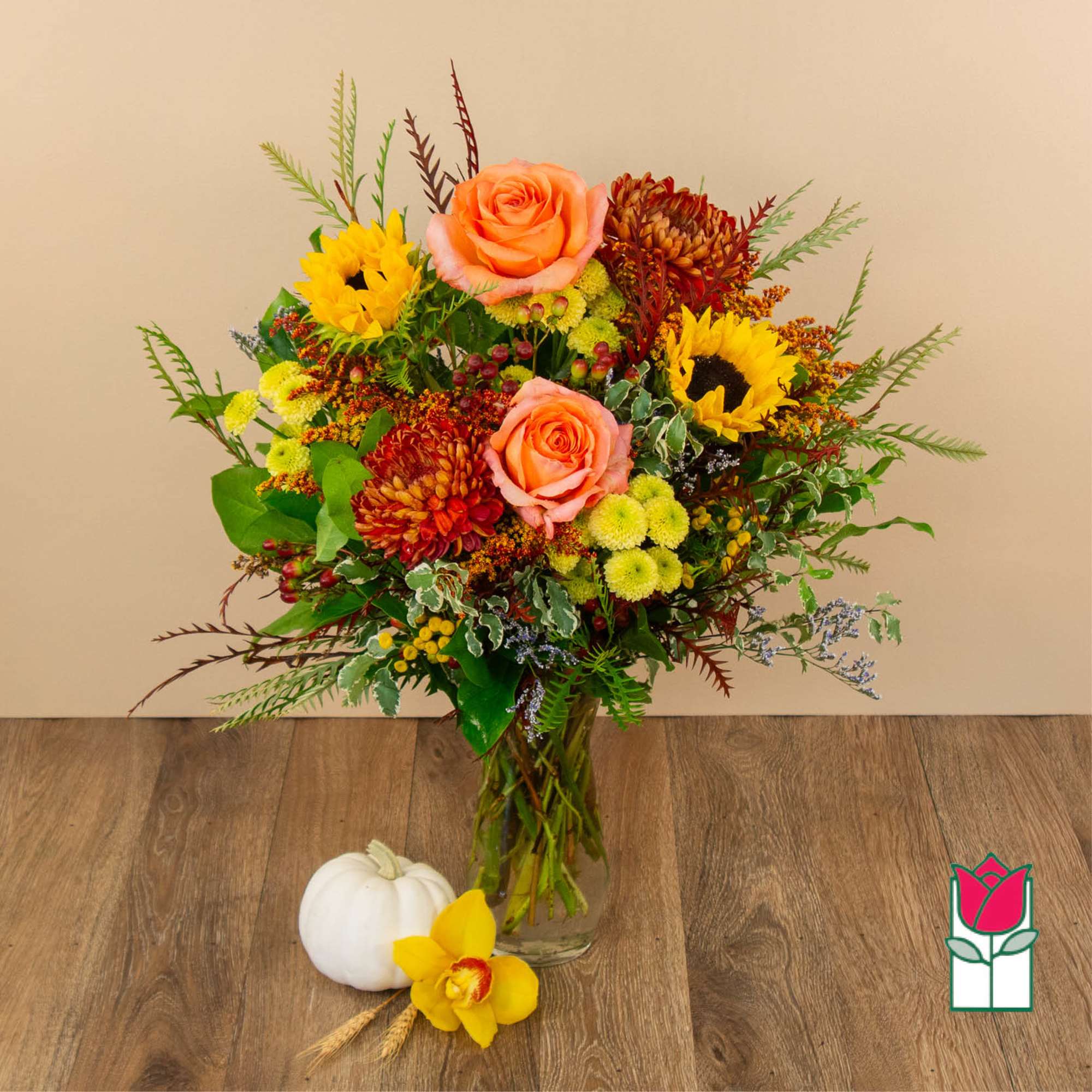 Mixed bouquet with peach roses, sunflowers, and chrysanthemums in a glass vase