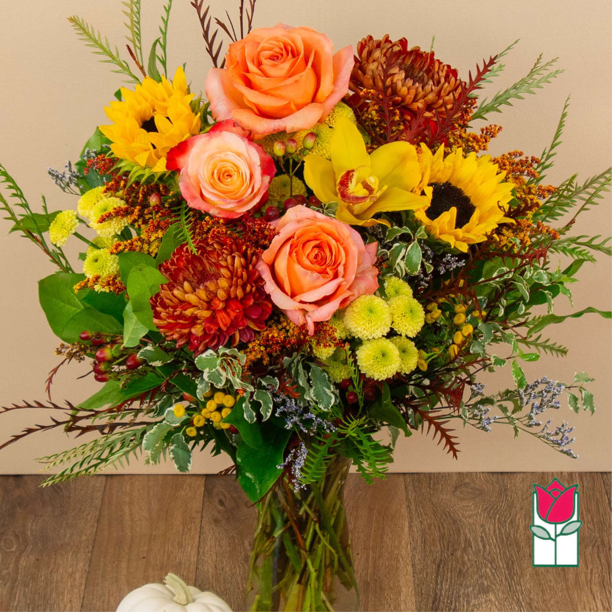 Mixed bouquet of roses, sunflowers, orchids, and mums in a glass vase