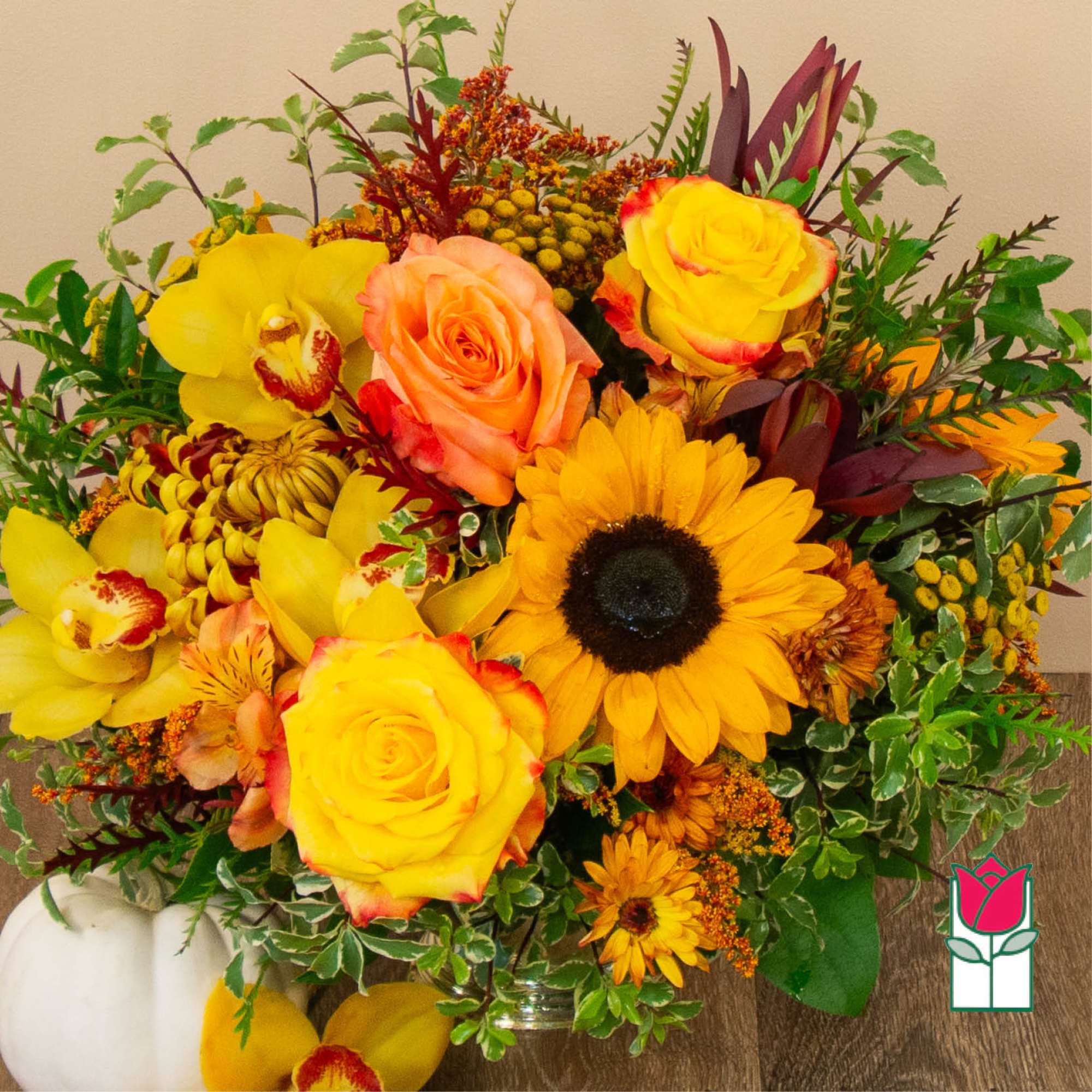 Bright mixed bouquet with yellow roses, orchids, and a sunflower in a glass vase