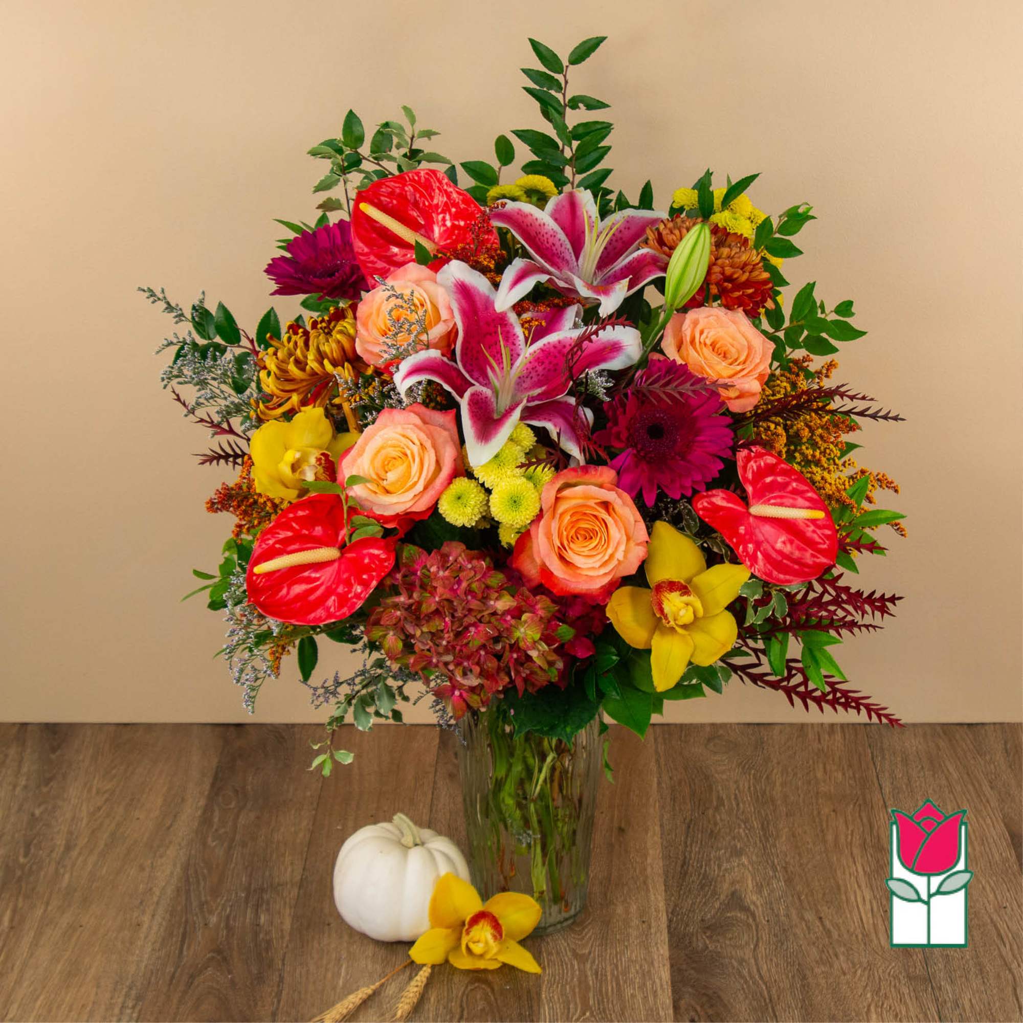 Mixed bouquet in a clear glass vase with lilies, roses, and bright tropical blooms
