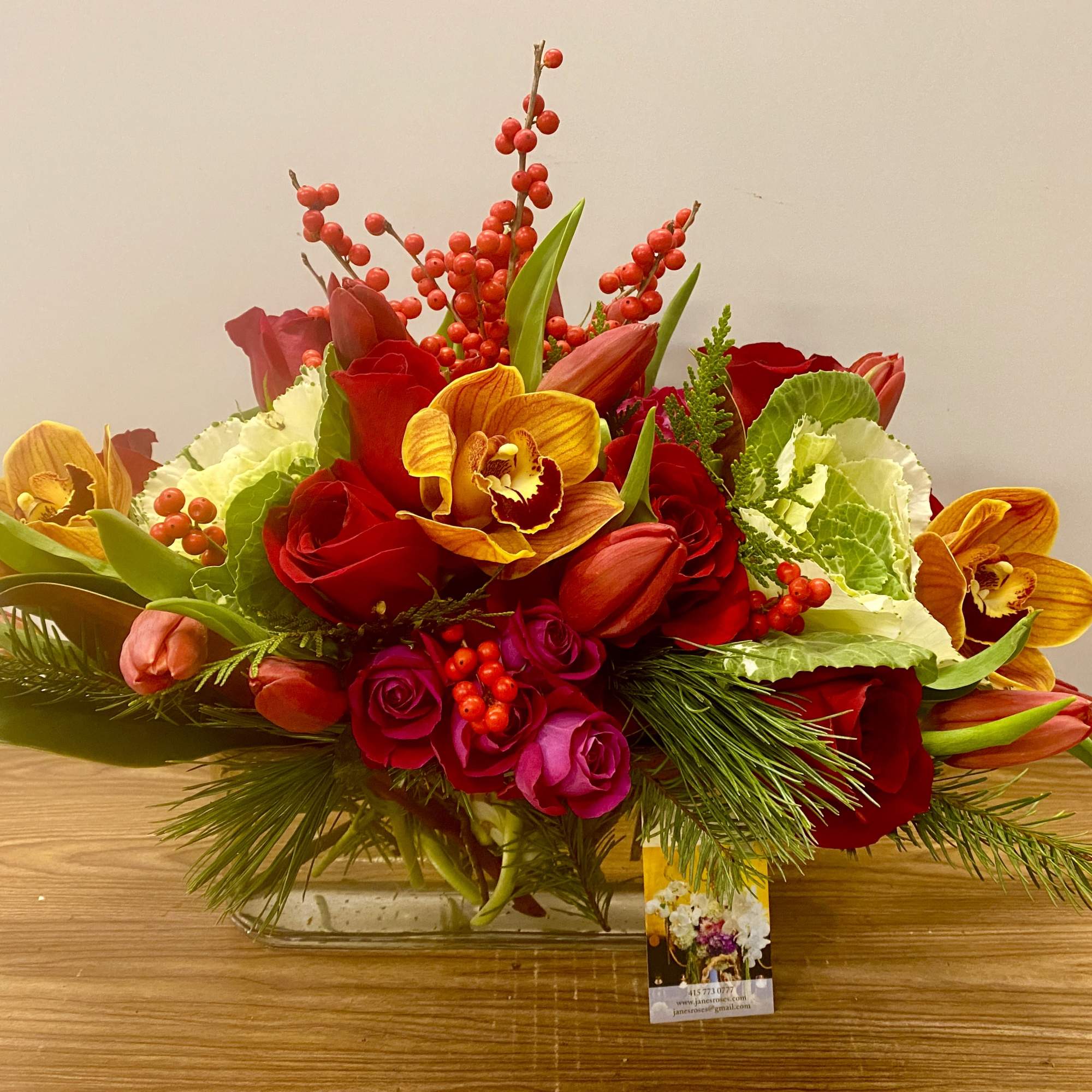 Mixed bouquet of red roses, tulips, and orange orchids in a glass vase