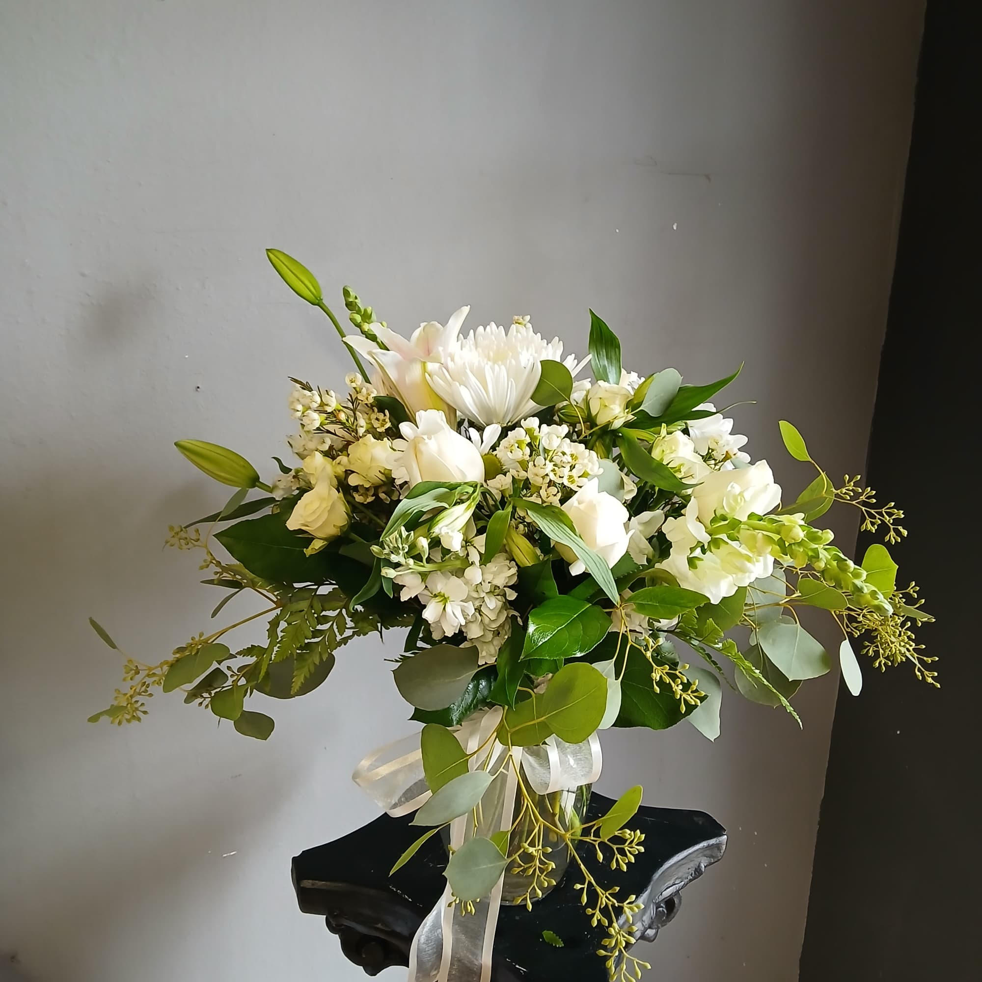 White floral arrangement in a glass vase with a ribbon
