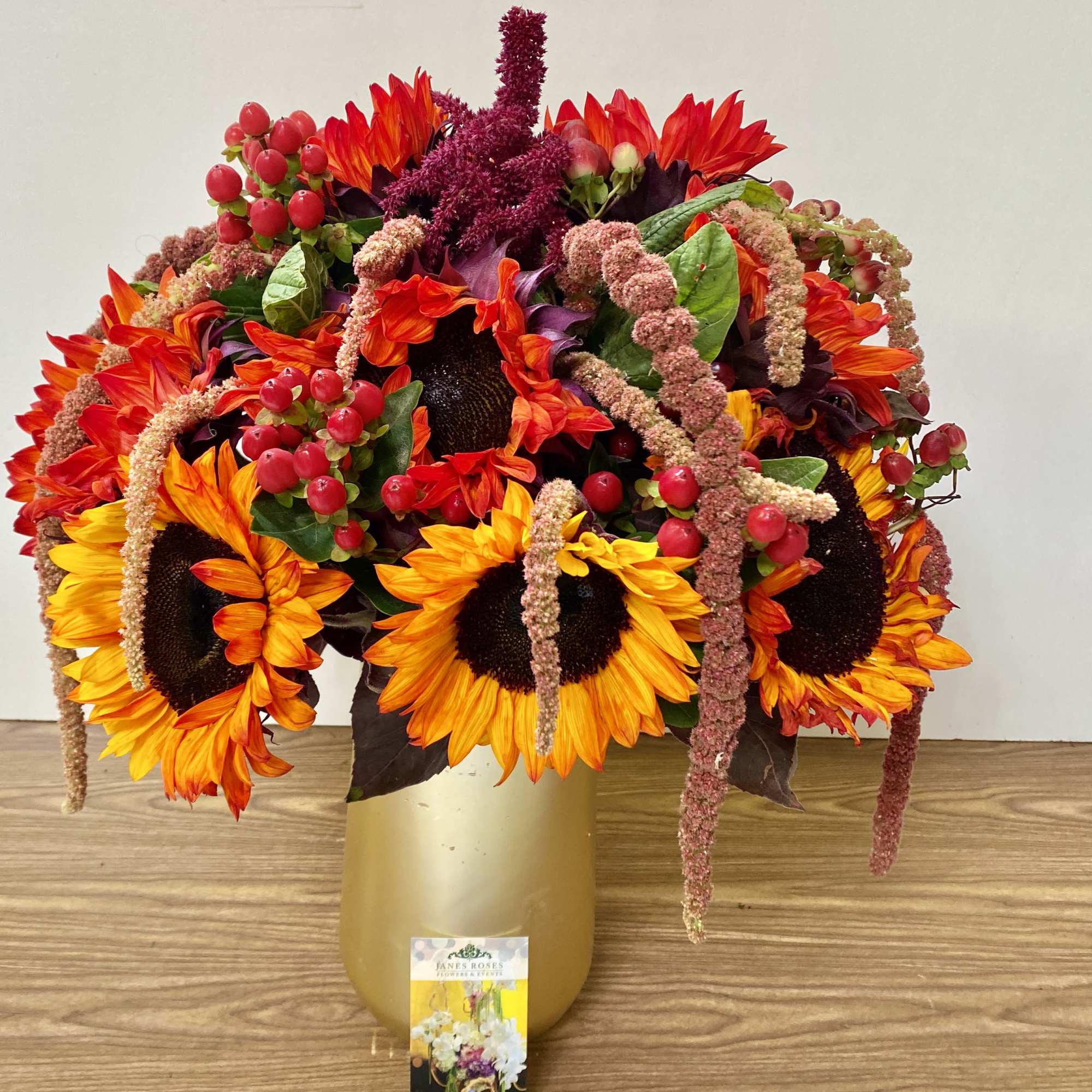 Sunflower arrangement in a gold vase with red berry accents