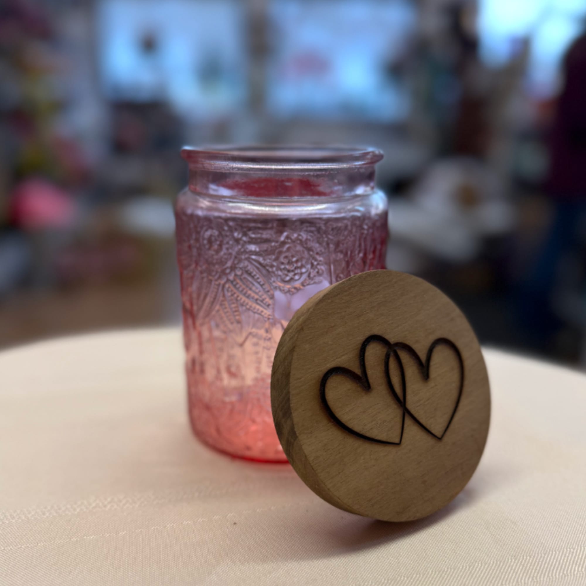 Pink glass jar candle with a wooden lid engraved with hearts
