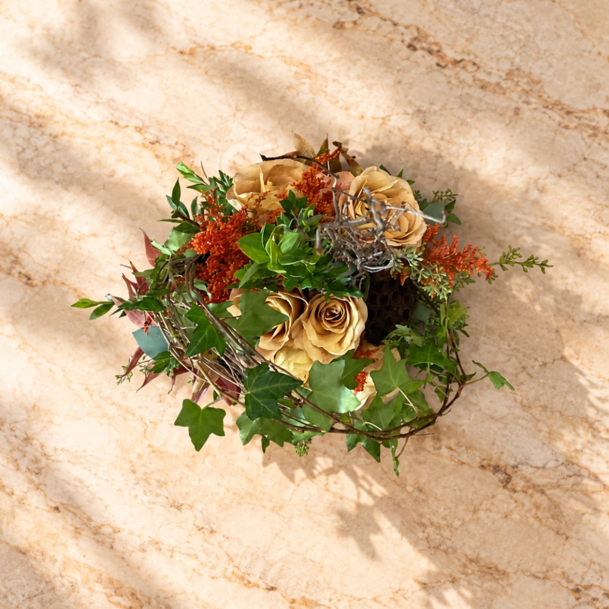 Small bouquet of beige roses with mixed greenery on a marble surface