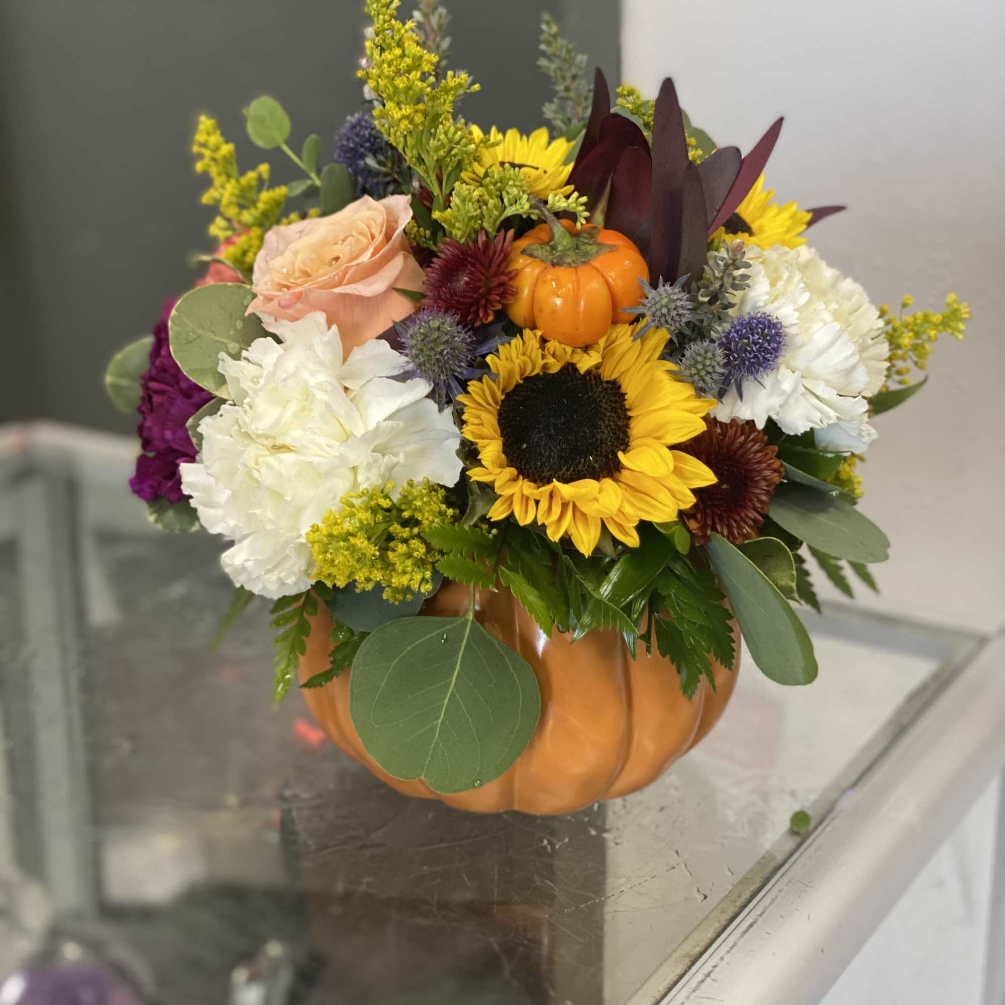 Fall bouquet in a pumpkin container with sunflowers, roses, and mums