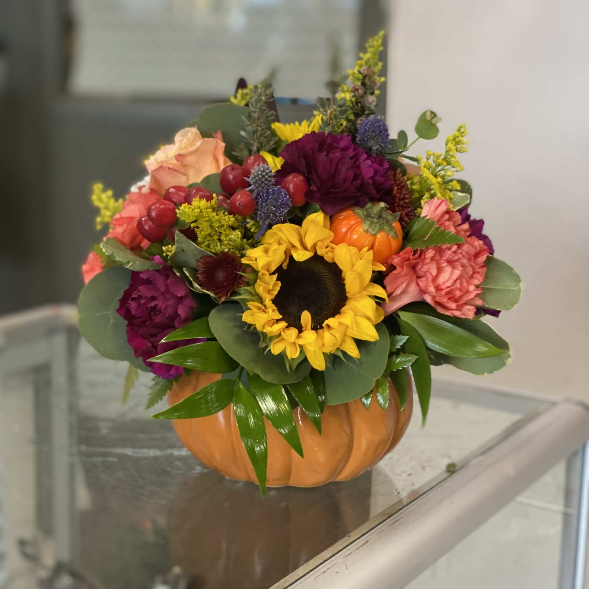 Mixed fall bouquet in a pumpkin-shaped container with a sunflower and roses