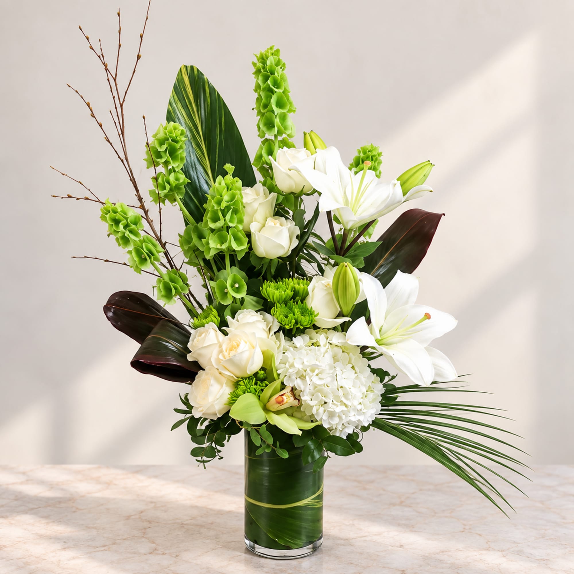 Tall white floral arrangement in a glass vase with green accents