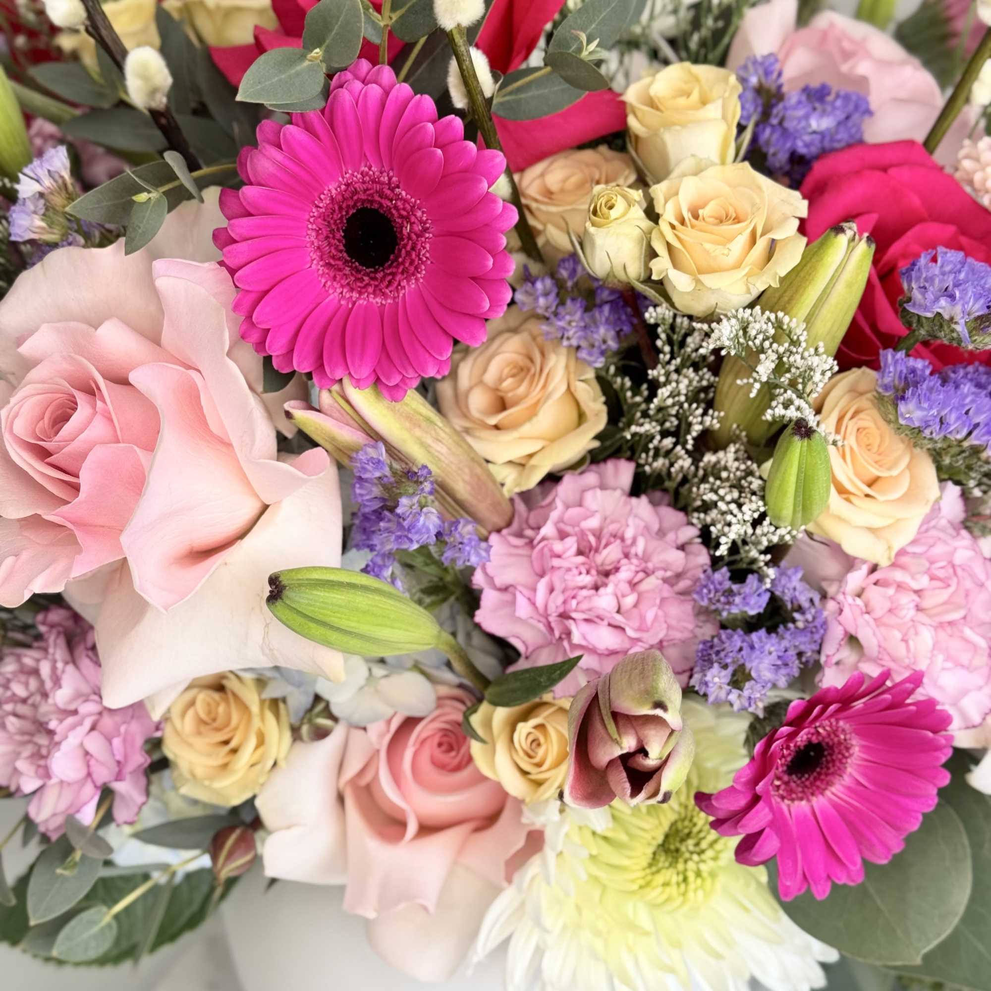 Rounded arrangement of pink gerbera daisies, roses, and mixed blooms in a white ceramic vase.