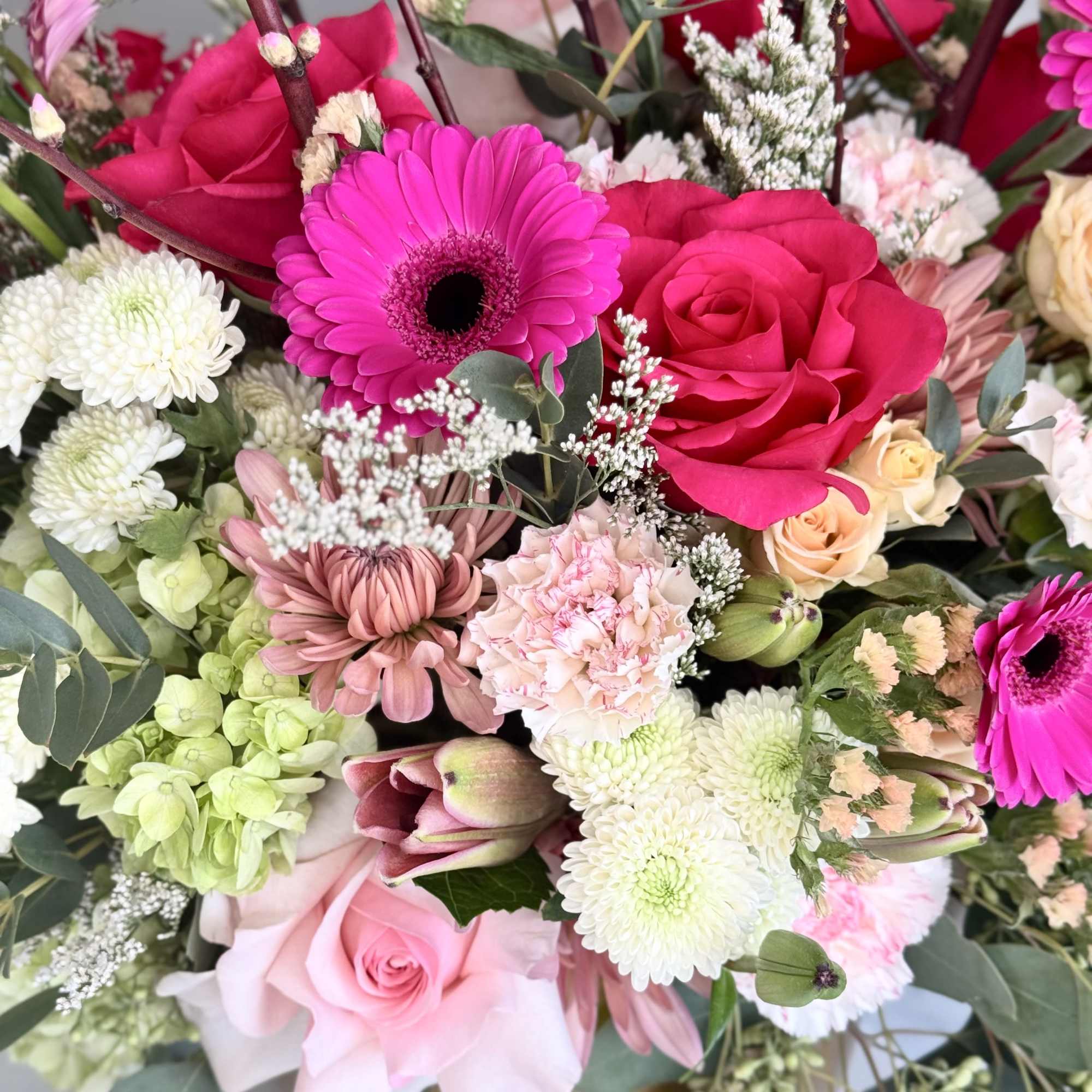 Mixed arrangement of pink roses, gerbera daisies, mums, and white blooms in a gold pot.