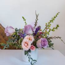 Compact arrangement of lavender roses and soft pink blooms in a white vase