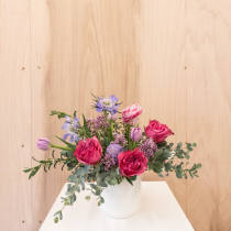Low arrangement of pink roses and purple tulips in a white vase on a white stand