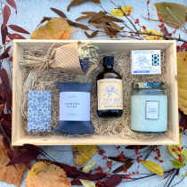 Wooden gift box with dried bouquet, candle, soaps, bubble bath, and comfort pack on autumn leaves