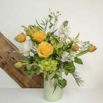 Tall arrangement of yellow roses, white flowers, green hydrangea and tulips in a pale vase