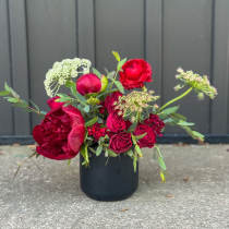 Low black vase with rich red roses and peonies accented by airy white blooms.