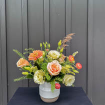Mixed bouquet of peach, cream, and orange flowers in a white ceramic vase