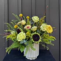 Green and yellow floral arrangement in a white vase