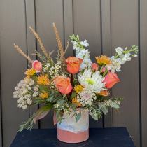 Mixed bouquet of peach roses, white blooms, and orange flowers in a ceramic vase