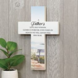 Cross-shaped memorial plaque with a Father’s tribute and a potted plant beside it