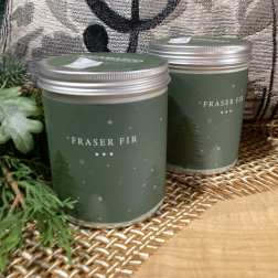 Two Fraser Fir candles in green tins with silver lids