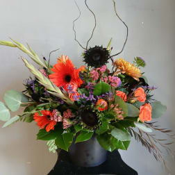 Mixed bouquet in a black vase with orange gerberas, roses, and dark sunflowers