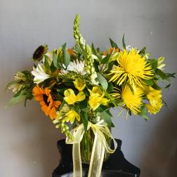 Mixed yellow, white, and orange flowers arranged in a glass vase with a ribbon