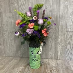 Halloween bouquet in a Frankenstein-themed vase with purple and orange flowers