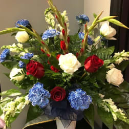 Red, white, and blue floral arrangement in a white pedestal vase