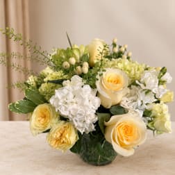 Cream and white rose bouquet in a glass vase with green accents