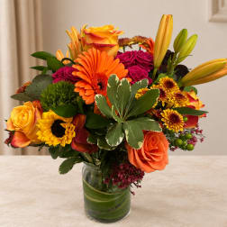Mixed bouquet of orange, yellow, and magenta flowers in a glass vase