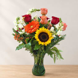 Mixed bouquet of roses, gerbera daisies, and sunflowers in a glass vase