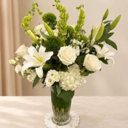 White lilies and roses in a clear glass vase with green accents