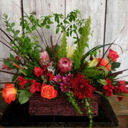 Mixed floral arrangement in a rectangular basket with red and orange blooms