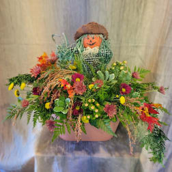 Fall floral arrangement with a scarecrow decoration in a pink container