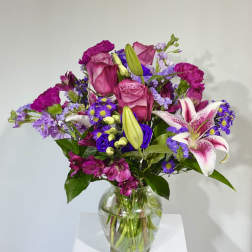 Bouquet of pink roses, lilies, and purple flowers in a glass vase