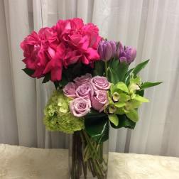 Pink roses, lavender roses, tulips, hydrangea, and green orchids in a glass vase