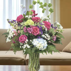 Mixed bouquet of pink roses, hydrangea, and purple flowers in a glass vase