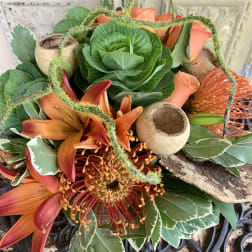 Orange lilies and a red-orange pincushion protea in a decorative arrangement