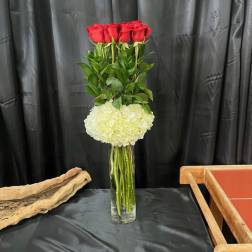Tall vase arrangement with red roses and a white hydrangea cluster