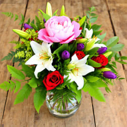 Bouquet of pink peonies, white lilies, and red roses in a glass vase