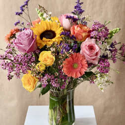 Mixed bouquet of roses, sunflower, and gerbera daisies in a glass vase