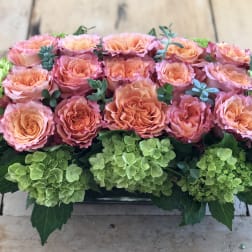 Peach and pink roses arranged with green hydrangeas in a low rectangular container
