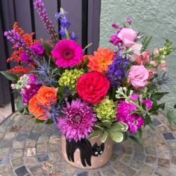 Bright mixed bouquet in a cat-decorated pot with pink, orange, purple, and green blooms.