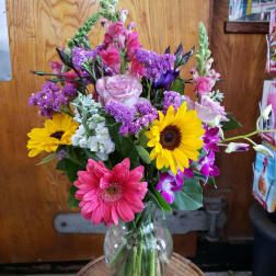 Mixed bouquet in a clear glass vase with pink, yellow, purple, and white flowers