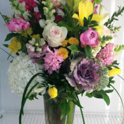 Tall mixed bouquet in a clear glass vase with pink, yellow, white, and purple flowers